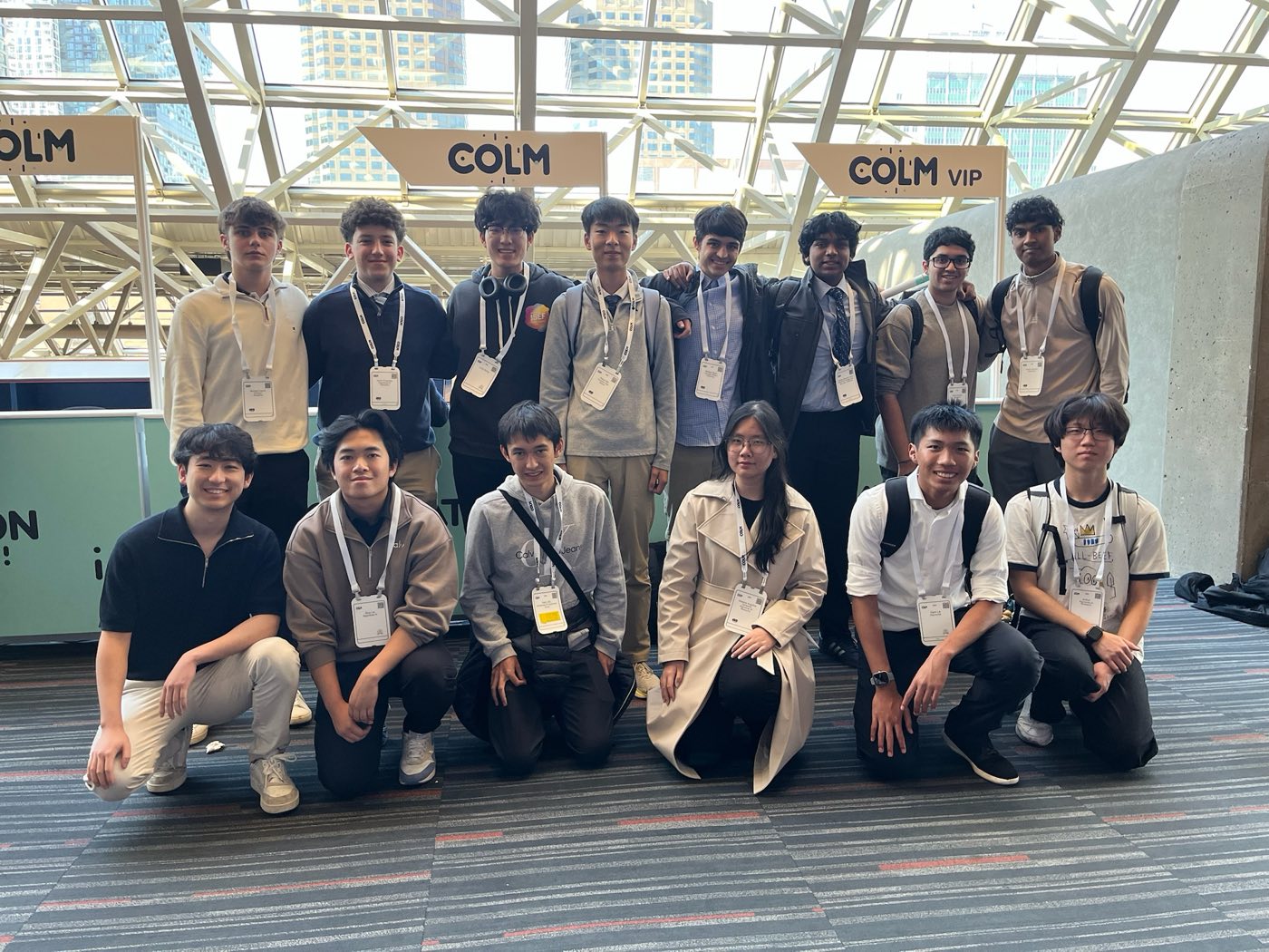 Algoverse student group photo in front of COLM 2025 conference banner